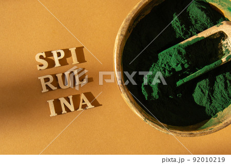 Blue-green algae spirulina powder in bamboo eco bowl with text SPIRULINA. Super powder in spoon. Food supplement source of protein and beta carotene 92010219