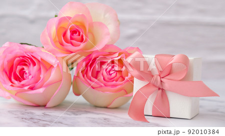 Gift box with tied ribbon bow pink roses on pink background. Greeting card. Present for springtime holidays Copy space for text. Gift box with tied ribbon bow pink roses on pink background. Greeting card. Present for springtime holidays Copy space for text. 92010384
