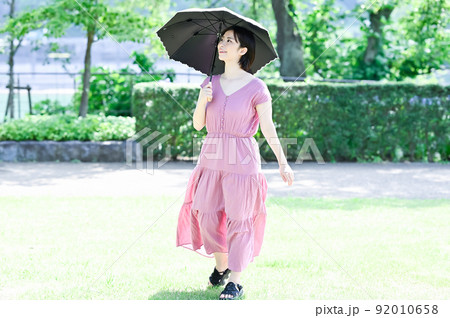 公園で日傘を差して散歩する女性 92010658