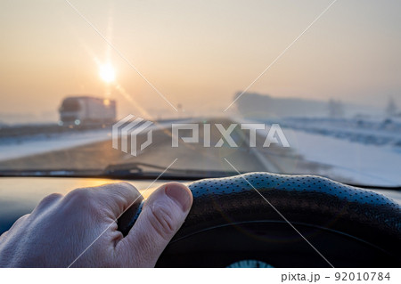 view of the driver hand on the steering wheel of the car while driving on a slippery snow covered road view of the driver hand on the steering wheel of the car while driving on a slippery snow covered road 92010784