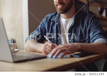 Hands of caucasian man with pen while taking notes at laptop at table. Male noting at computer. 92011185