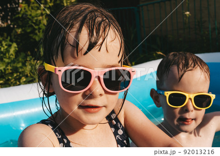 Portrait of happy kids in sunglasses in swimming pool Portrait of happy kids in sunglasses in swimming pool 92013216
