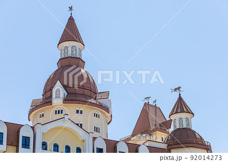 Towers with weathercocks of a building made in the style of a fairy-tale castle against the blue sky. Hotel Bogatyr Towers with weathercocks of a building made in the style of a fairy-tale castle against the blue sky. Hotel Bogatyr 92014273