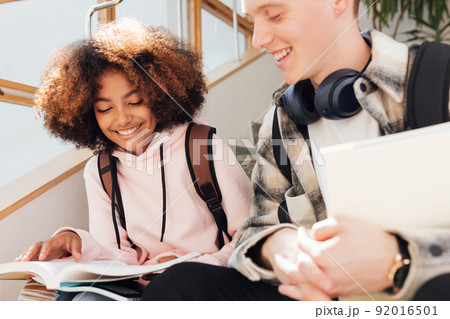 Cropped shot of two classmates sitting on stairs preparing assignments and smiling 92016501