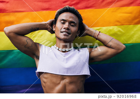 Guy posing on LGBT flag. Laughing male standing against rainbow flag. Guy posing on LGBT flag. Laughing male standing against rainbow flag. 92016968