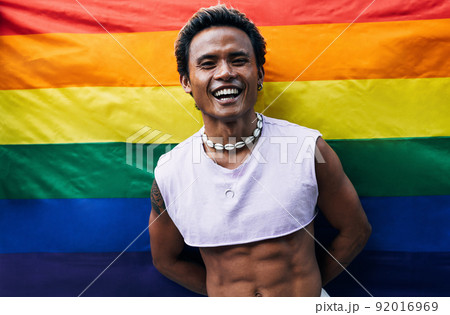Guy posing on LGBT flag. Laughing male standing against rainbow flag.	 92016969