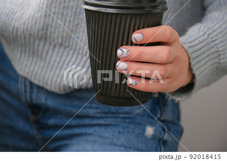 Manicured female hands holding black eco recycling coffee cup with stylish blue nails and minimalistic design. Trendy modern design manicure. Gel nails. Skin care. Beauty treatment. Nail care Manicured female hands holding black eco recycling coffee cup with stylish blue nails and minimalistic design. Trendy modern design manicure. Gel nails. Skin care. Beauty treatment. Nail care 92018415