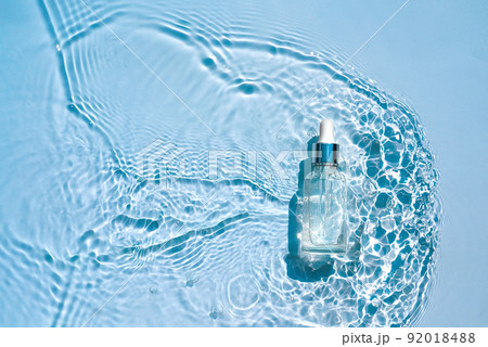 Moisturizing cosmetic serum in transparent bottle with a dropper in water waves, blue background Moisturizing cosmetic serum in transparent bottle with a dropper in water waves, blue background 92018488
