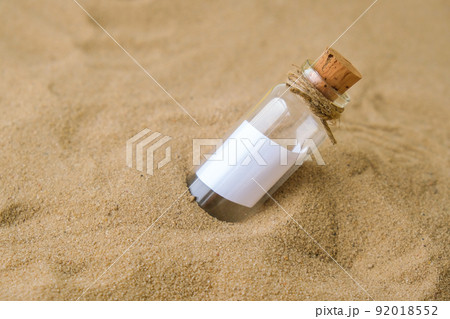Letter in a bottle on the beach. Island lifestyle. Paper Message in a glass bottle with a cork on the sand. Note on salvation, please help. SOS concept. Copy space 92018552