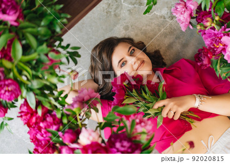 an attractive young woman in a pink blouse with peony flowers on the floor. an attractive young woman in a pink blouse with peony flowers on the floor. 92020815