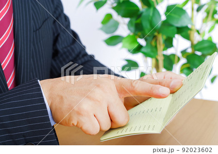 貯金通帳に指を刺して確認する男性 92023602