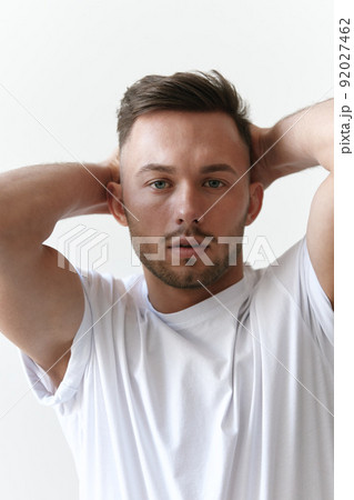 Closeup portrait shot of handsome tanned man guy in basic t-shirt holds hands behind head looks at camera posing on white background. Fashion Style New Collection Offer. Copy space for ad. Model snap Closeup portrait shot of handsome tanned man guy in basic t-shirt holds hands behind head looks at camera posing on white background. Fashion Style New Collection Offer. Copy space for ad. Model snap 92027462