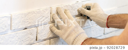 A professional builder sticks decorative tiles on the wall. A worker mounts a decorative brick on a wall 92028729