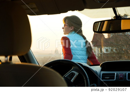 Young woman standing near her car enjoying warm sunset view. Girl traveler leaning on vehicle hood looking at evening horizon. Young woman standing near her car enjoying warm sunset view. Girl traveler leaning on vehicle hood looking at evening horizon. 92029107