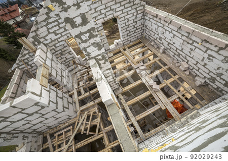 View from above of future multi stored cottage energy saving walls of large white hollow foam insulation blocks and temporary wooden scaffolding frame. Construction masonry, modern technology concept. View from above of future multi stored cottage energy saving walls of large white hollow foam insulation blocks and temporary wooden scaffolding frame. Construction masonry, modern technology concept. 92029243
