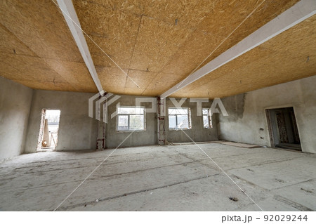 Unfinished apartment or house big loft room under reconstruction. Plywood ceiling, plastered walls, window openings, cement floor. Construction and renovation concept. Unfinished apartment or house big loft room under reconstruction. Plywood ceiling, plastered walls, window openings, cement floor. Construction and renovation concept. 92029244