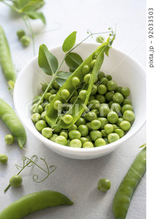 Green fresh peas, snack pea in a white bowl on a neutral grey background. Top view. Summer garden vegetables. 92033503