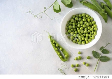 Green fresh peas, snack pea in a white bowl on a neutral grey background. Top view. Summer garden vegetables. 92033504