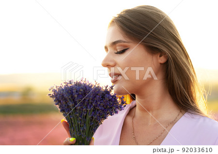 Close up portrait of a young woman holding bouquet of lavender whiile standing in lavender field 92033610