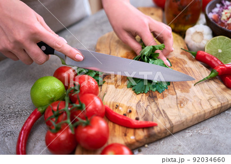 making salsa dip sauce - woman cutting and chopping cilantro or parsley on wooden cutting board making salsa dip sauce - woman cutting and chopping cilantro or parsley on wooden cutting board 92034660