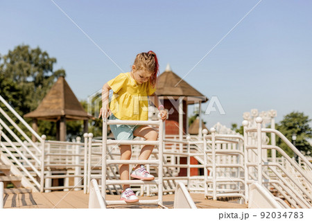 A charming little girl is having fun and playing on the playground. Happy childhood, summer time 92034783