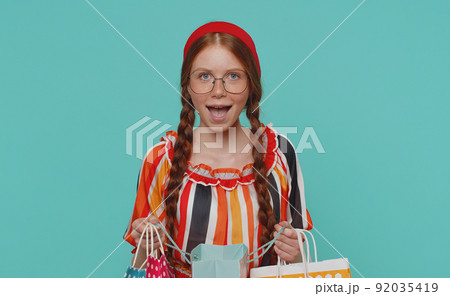 Ginger girl showing shopping bags, advertising discounts, smiling looking amazed with low prices Ginger girl showing shopping bags, advertising discounts, smiling looking amazed with low prices 92035419