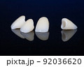 four dental crowns zirconia on a mirror table, black background. crowns for front teeth. 92036620