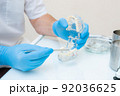 hands of a dentist in blue gloves close-up. dentist with tweezers shows defects on the acrylic model of the jaw. 92036625