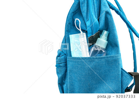 Close up side pocket of blue student backpack with face mask and a small bottle of alcohol, side view backpack, isolated image on white background. Concept of back to school in the era of the virus. 92037333