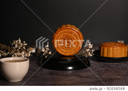 Chinese traditional mid autumn festival moon cake with cup of tea and dried flowers on black stone table Chinese traditional mid autumn festival moon cake with cup of tea and dried flowers on black stone table 92038568