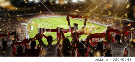 Back view of football, soccer fans cheering their team with colorful scarfs at crowded stadium at evening time. Concept of sport, support, competition. Out of focus effect 92040543