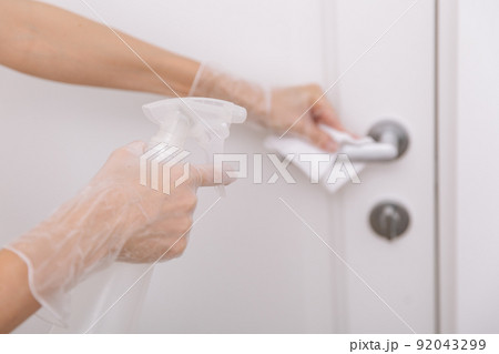 Cleaning door handles with wet wipe and white gloves. Sanitize surfaces prevention in hospital and public spaces against corona virus. Woman hand using towel for cleaning home room door link. 92043299