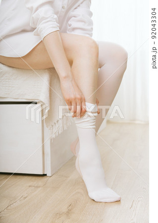 Girl putting on white stockings at home. Anti-embolic stockings. Compression Hosiery. Medical stockings, tights, socks, calves and sleeves for varicose veins and venouse therapy. Girl putting on white stockings at home. Anti-embolic stockings. Compression Hosiery. Medical stockings, tights, socks, calves and sleeves for varicose veins and venouse therapy. 92043304