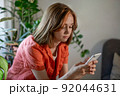 Young female using smartphone at home checking email, writing message in social network, searching information.  92044631