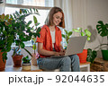 Young female using laptop at home checking email, writing message in social network, searching information. Cozy workplace, remote work learning concept. 92044635