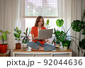 Young female using laptop at home checking email, writing message in social network, searching information. Cozy workplace, remote work learning concept. 92044636