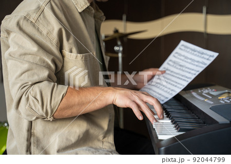 Young man checks music sheet and plays notes on synthesizer 92044799