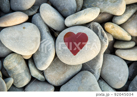 stone heart painted with a red paint marker on the pebble as a gift for Saint Valentine day on the pebble background. 92045034