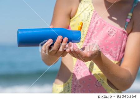 Girls hand squeezing out sunscreen on her hand. 92045364
