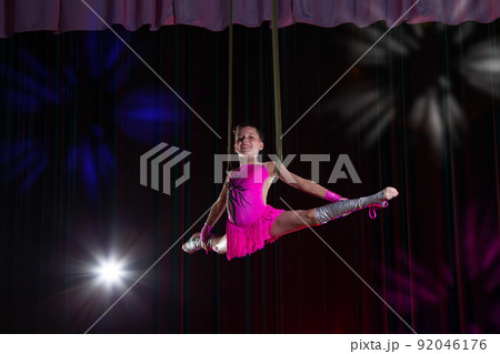 Circus artist acrobat performance. The girl performs acrobatic elements in the air. Circus gymnast on the stage Circus artist acrobat performance. The girl performs acrobatic elements in the air. Circus gymnast on the stage 92046176