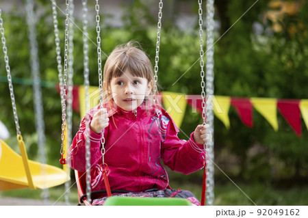 A little girl in a red jacket sits on a chain carousel ride. 92049162