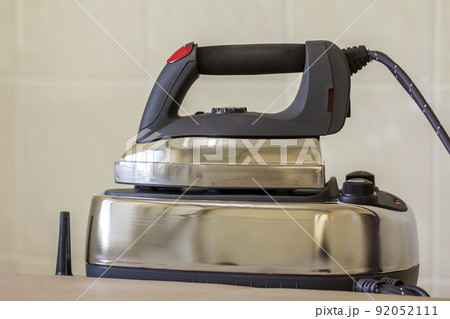 Close-up of new modern stainless steel iron with teflon sole and with steam generator isolated on iron plate on light copy space background. Close-up of new modern stainless steel iron with teflon sole and with steam generator isolated on iron plate on light copy space background. 92052111