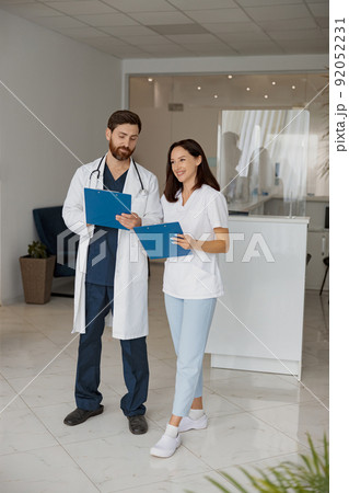 Two doctor colleagues discussing patient diagnosis stand in clinic hall 92052231