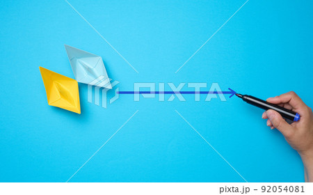 Two paper boats and a woman's hand with a marker on a blue background. The concept of indicating the way forward. Two paper boats and a woman's hand with a marker on a blue background. The concept of indicating the way forward. 92054081