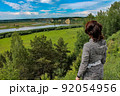 A girl standing on a hill, on a steep bank of a river in summer and looking into far away. 92054956