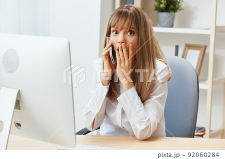 Excited adorable blonde businesswoman worker make difficult decision talking with client in call in light modern office. Nervous employee work on computer online in support service. Copy space 92060284