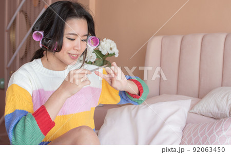 Portrait of asian woman rolling her hair and brushing her nails in pink bedroom 92063450