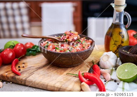 freshly made salsa dip sauce - chopped garlic, tomatoes and onion in wooden bowl 92065115
