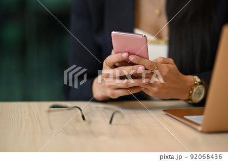 Cropped view of working woman using mobile phone, communicating in social media Cropped view of working woman using mobile phone, communicating in social media 92068436