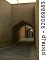 A narrow street with adobe houses in the old city of Yazd, which barely fit people and a car 92069883